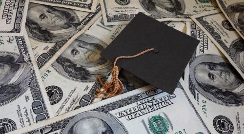 Small black graduation cap on top of hundreds of dollars of student loans