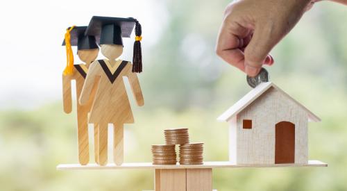 Wooden figurines in graduation caps balanced on scale with house