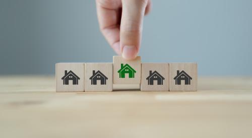 Wooden blocks with gray houses and one green house that represents sustainability