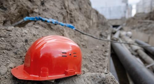 Red construction hard hat in trench 