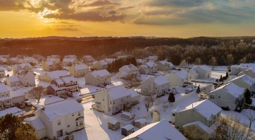 Aerial view of sun rising above snowy neighborhood