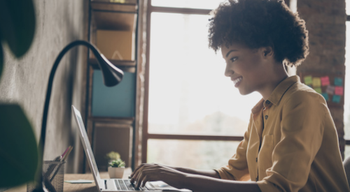 Woman sitting at desk in home office working on laptop. 