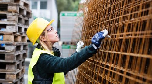 Woman wearing blue hard hat installing tile in wall 