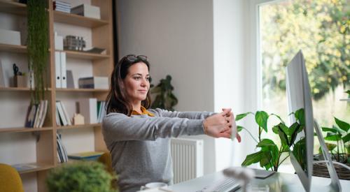 woman sitting at desk stretching shoulders as she works from home